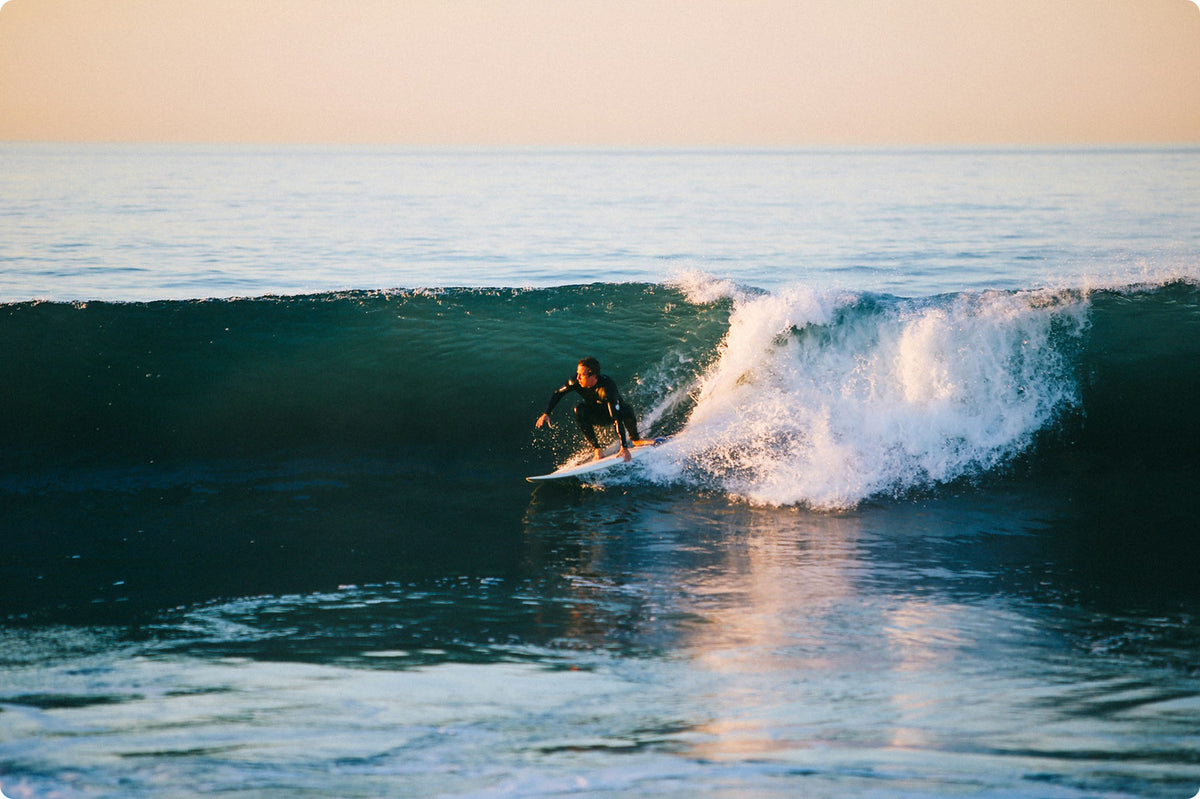 Person surfing on a wave with a sunset in the background